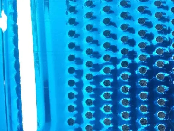 Close-up of a blue rectangular kitchen tool with a series of evenly spaced small, circular indentations in a grid pattern. The surface has a slightly glossy, reflective appearance with a vertical white light reflecting along the left edge, reminiscent of a sleek Techmanistan 3in1 Stainless Steel Vegetable Slicer Chopper Grater.