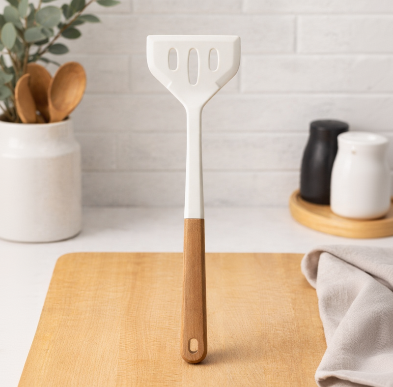 White spatula with wooden handle on a wooden cutting board in a kitchen setting.